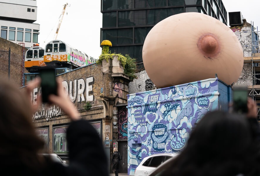 A wide angle of a London landscape. A giant inflatable boob on one of the buildings.