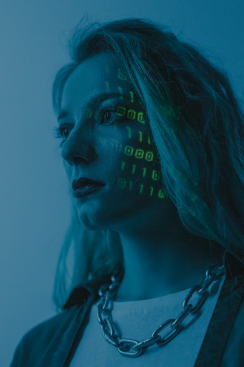 A close-up of a young white woman. Lines of coding projected on the right half of her face.