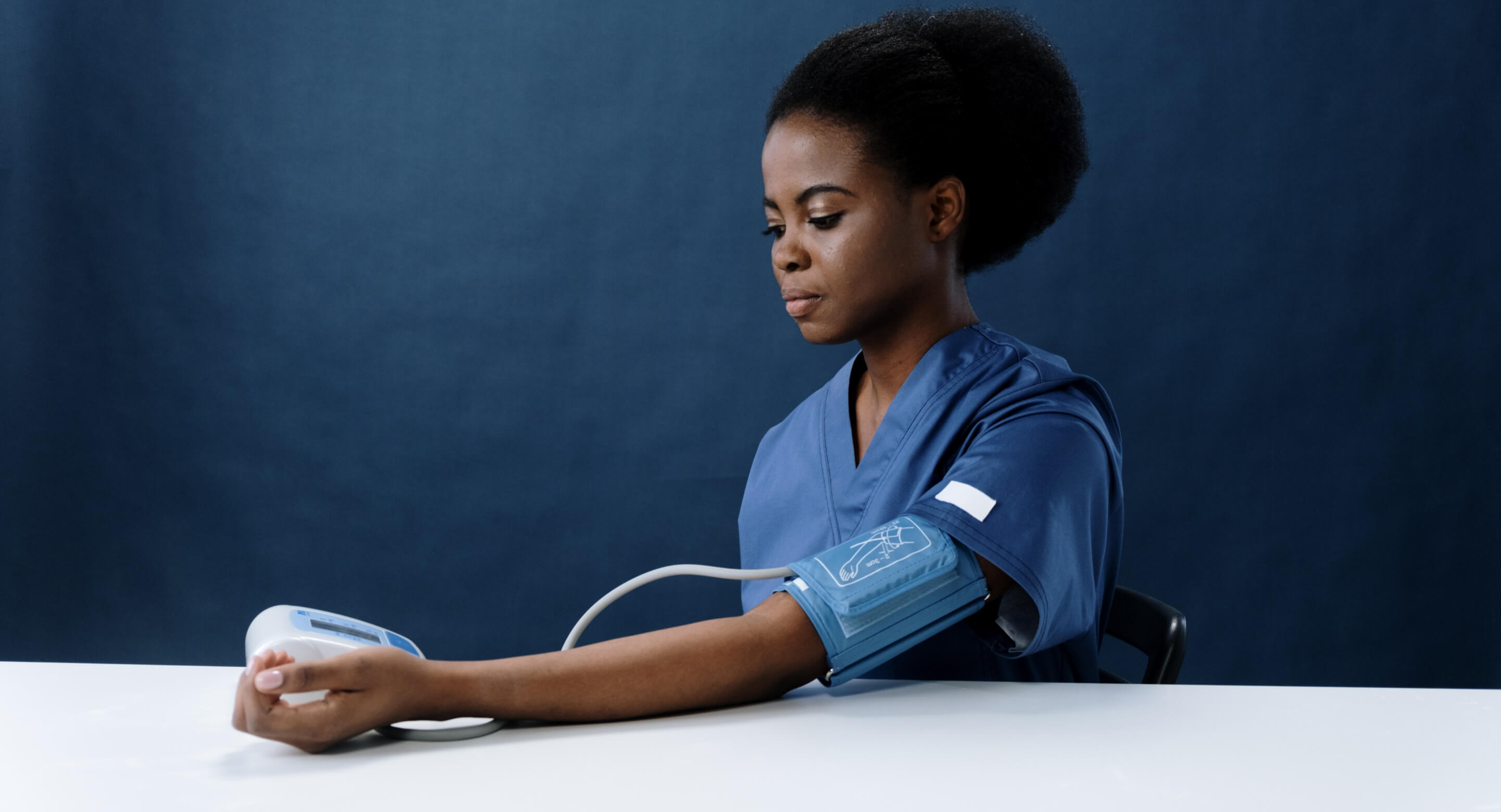 A black woman in a nurse uniform, checking her blood pressure using a MedTech device.