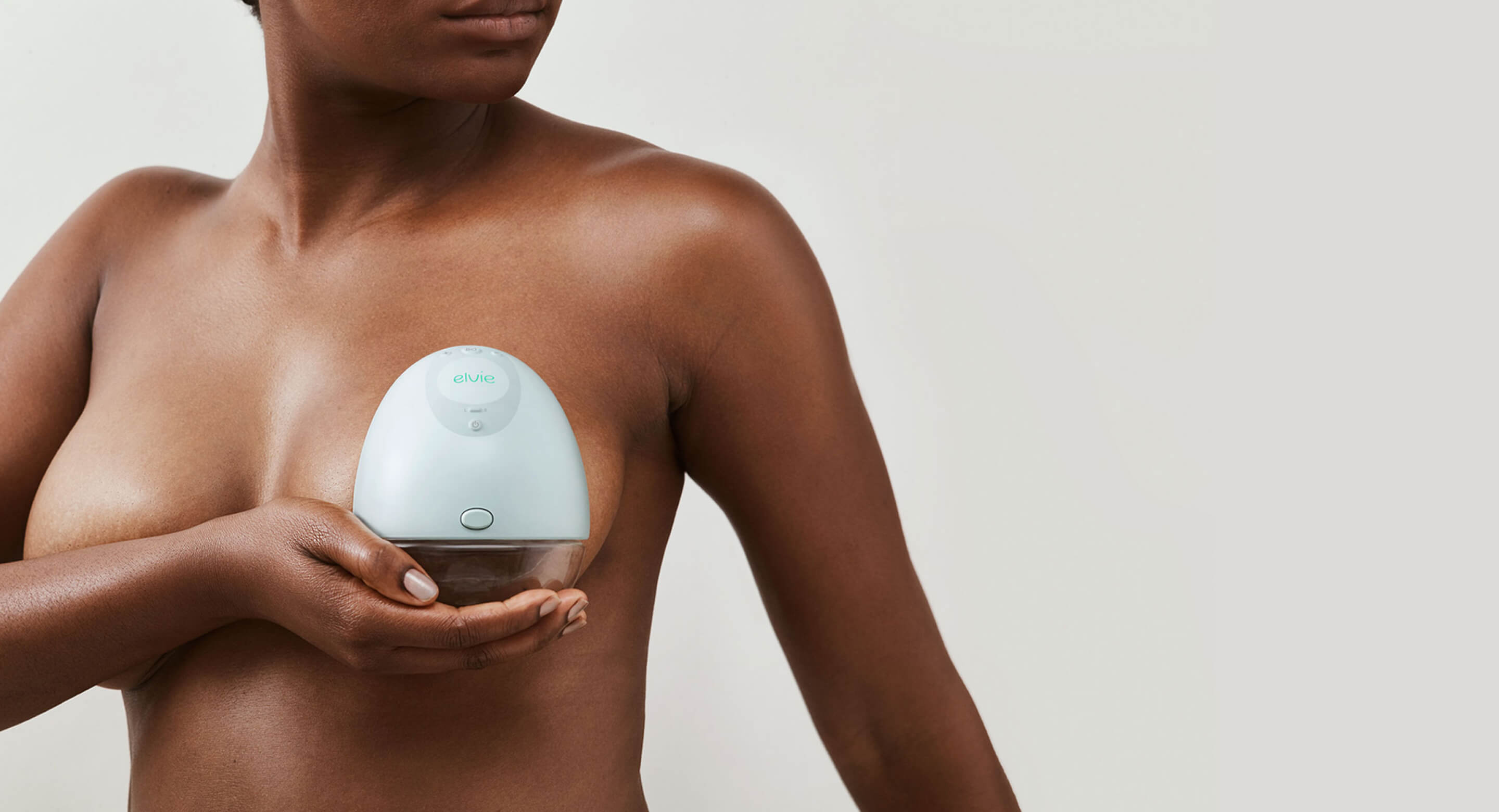 A close-up of one side of a black woman's chest. A model is holding a device covering her breast. The device is Elvie Pump - a wireless smart breast pump.