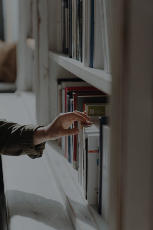 A close-up of a hand reaching out for a book from a bookshelf.
